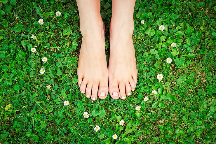 Person standing barefoot on grass — the health benefits of grounding and earthing, Earth Aya Energy