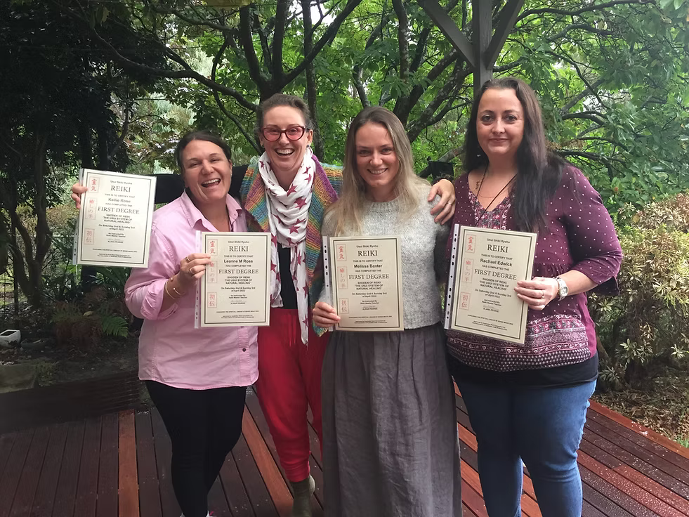 Four joyful Reiki Level 1 graduates proudly holding their certificates on the deck at Earth Aya Energy, Healesville, surrounded by lush green garden