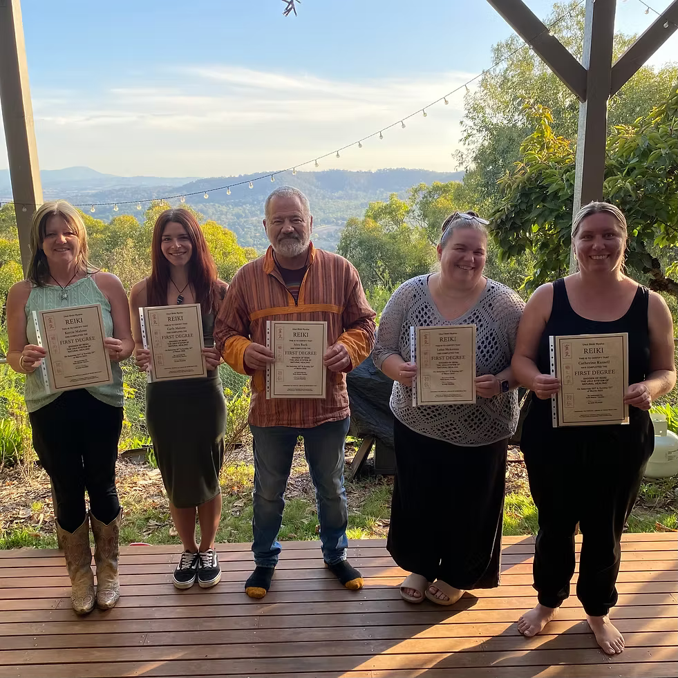Five Reiki Level 1 graduates proudly holding their certificates on the deck at Earth Aya Energy, Healesville, with Yarra Valley views in the golden afternoon light
