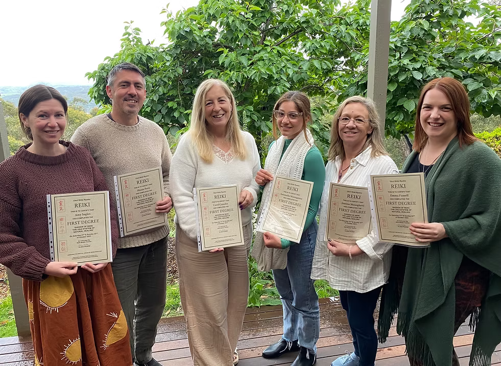 Six Reiki Level 1 graduates proudly holding their certificates on the deck at Earth Aya Energy, Healesville, surrounded by lush garden greenery
