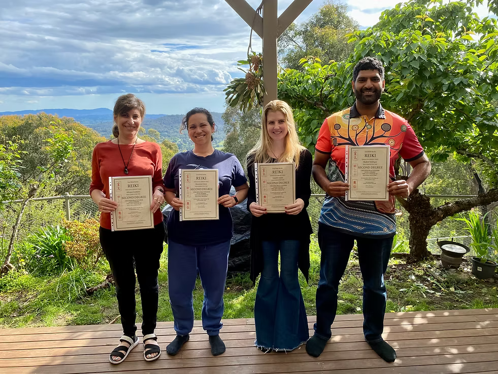 Four Reiki Level 2 graduates proudly holding their certificates on the deck at Earth Aya Energy, Healesville, with lush garden greenery and Yarra Valley views in the background