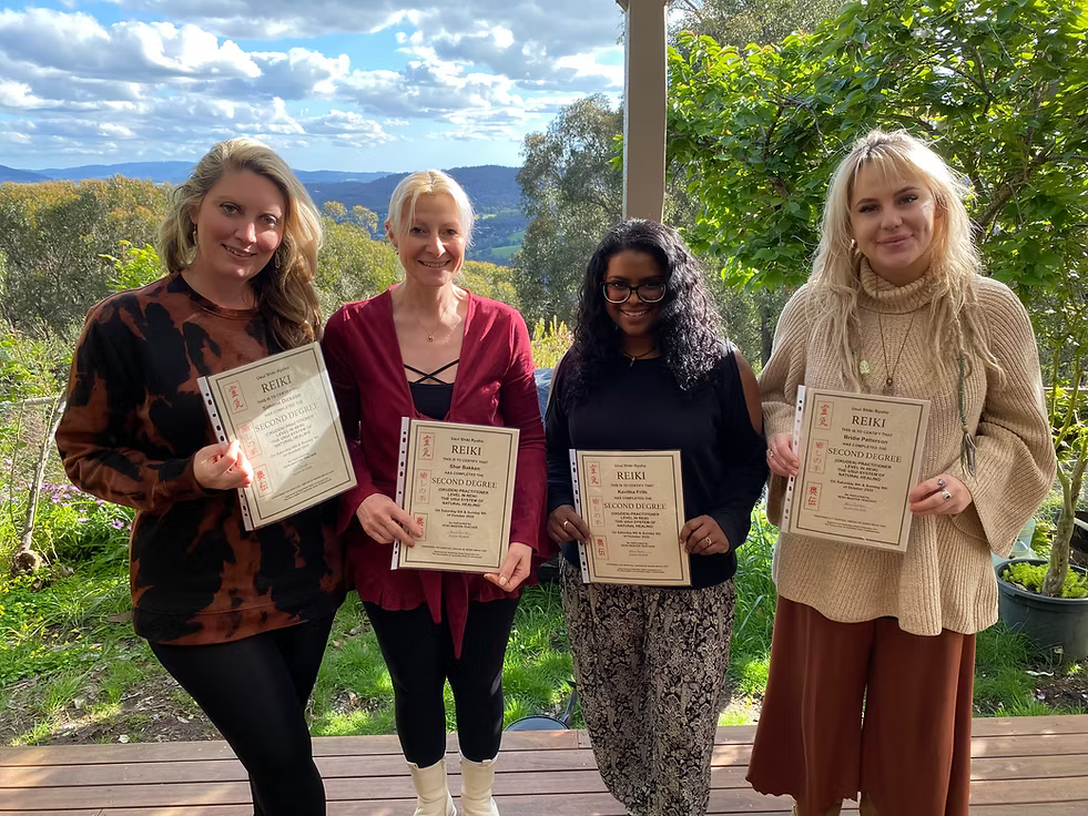 Four Reiki Level 2 graduates proudly holding their certificates on the deck at Earth Aya Energy, Healesville, with beautiful Yarra Valley views and blue skies in the background