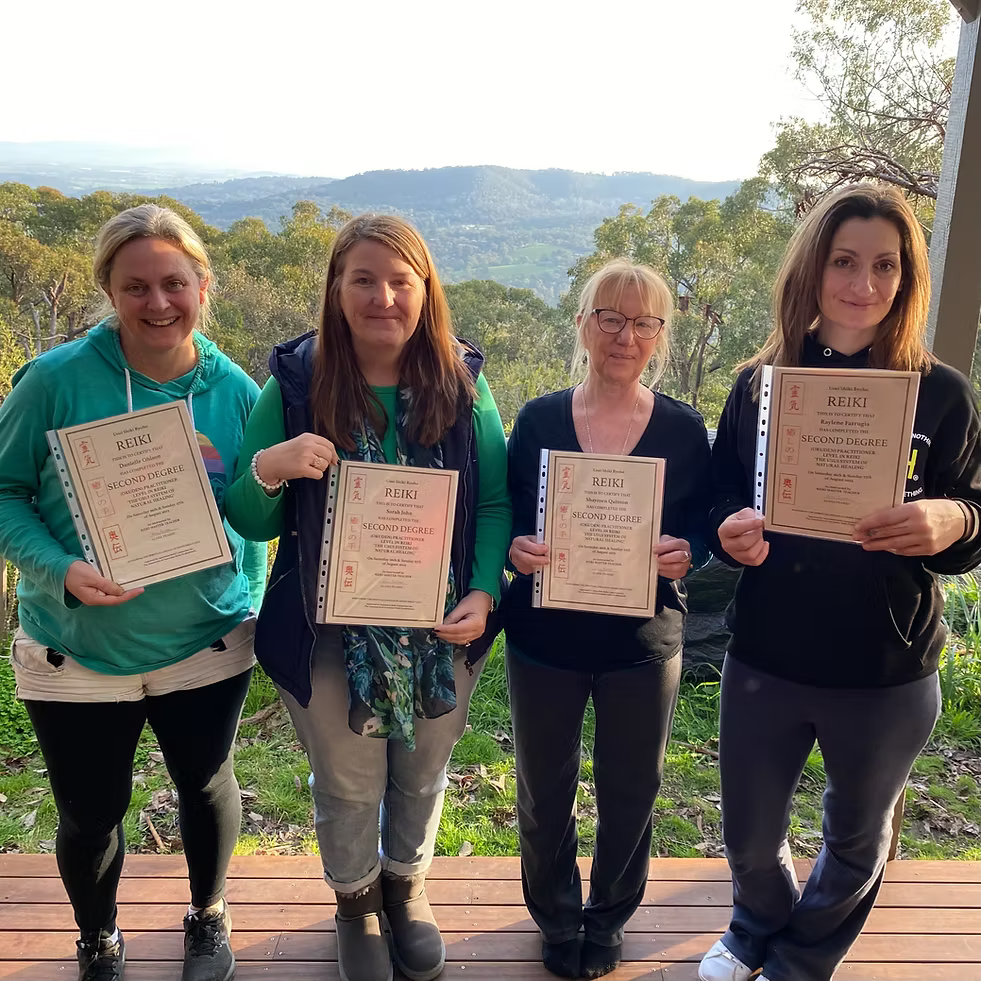 Four Reiki Level 2 graduates proudly holding their certificates on the deck at Earth Aya Energy, Healesville, with sweeping Yarra Valley views in the background