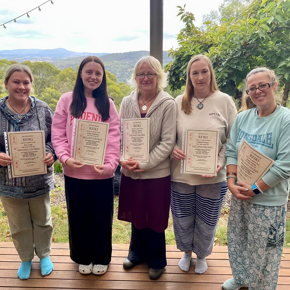 Five Reiki Level 2 graduates proudly holding their certificates on the deck at Earth Aya Energy, Healesville, with Yarra Valley views in the background