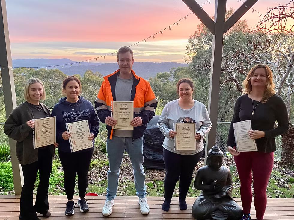 Five Reiki Level 2 graduates proudly holding their certificates on the deck at Earth Aya Energy, Healesville, with a stunning Yarra Valley sunset in the background