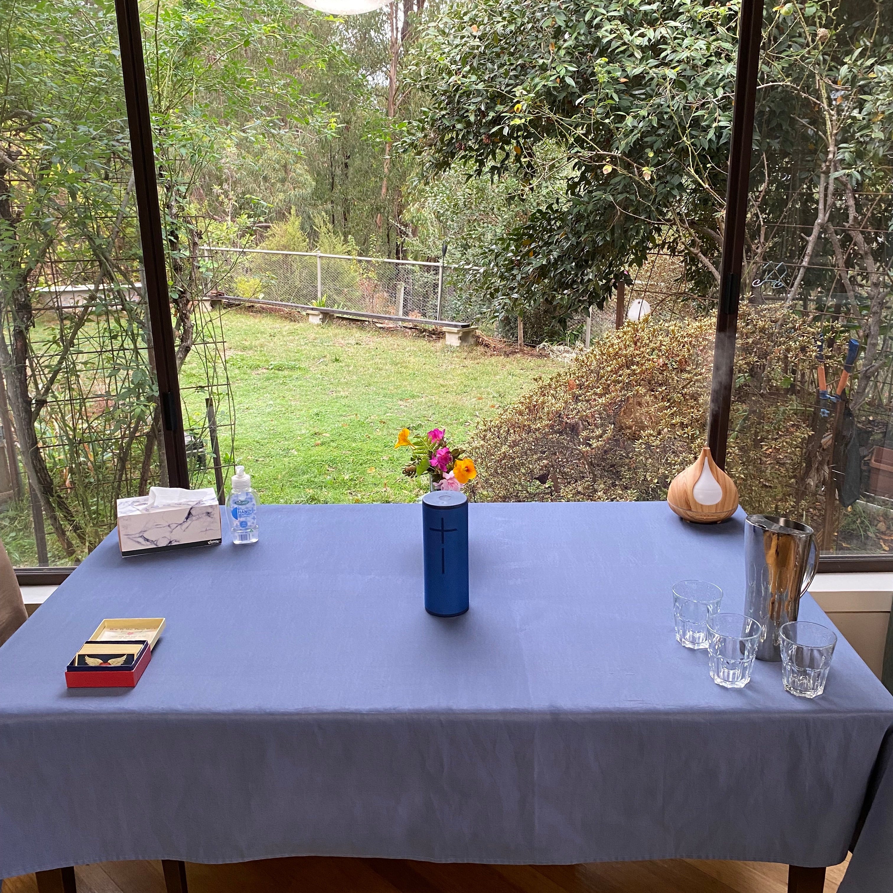 Welcoming table set up for a Reiki Share class at Earth Aya Energy — angel cards, music speaker, flowers, essential oil diffuser, and water for students, with a view of the garden in Healesville
